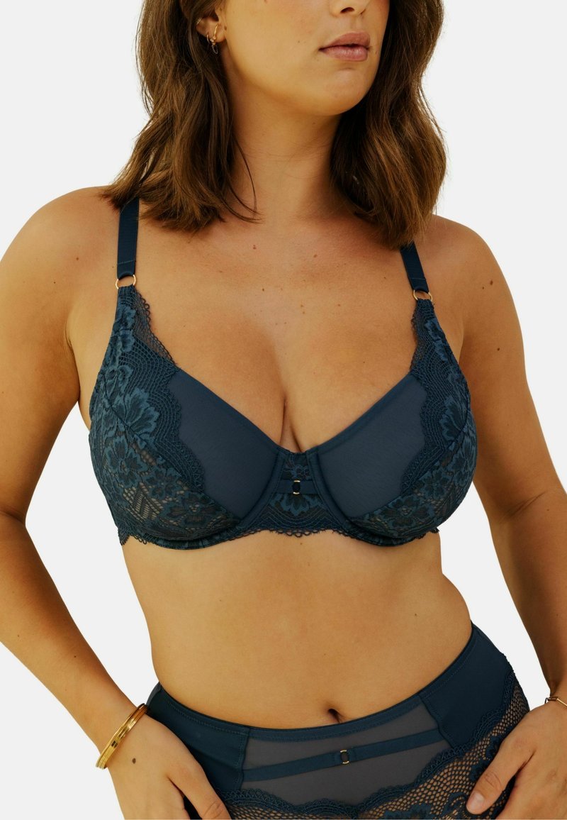 Soutien-gorge en dentelle marine avec motif floral, superposition en maille semi-transparente, soutien-gorge à armatures, bretelles ajustables et ornements décoratifs centraux.