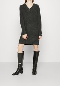 Abito maglione lavorato a maglia di colore grigio scuro con scollatura a V, maniche lunghe e spacchi laterali. Abbinato a stivali neri in pelle con tacco alto e punta quadrata.