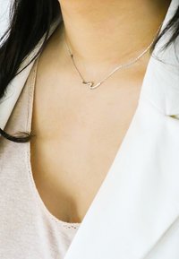 Silberne Halskette an einer filigranen Kette mit einem gewellten Anhängerdesign. Die Kette ist dünn und betont den minimalistischen Stil.