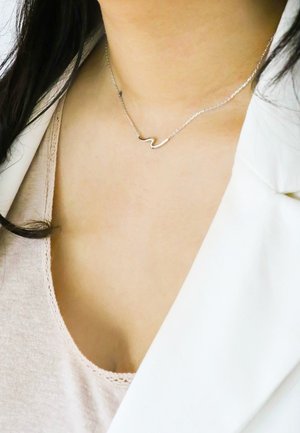 Zilveren ketting op een delicate schakel met een golvende hangerontwerp. De ketting is dun, waardoor de minimalistische stijl extra wordt benadrukt.