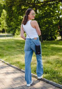 Pair of light blue wide-legged jeans, white tank top, and white sneakers. A black crossbody bag with pink accents hangs from a chain.
