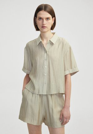 Camicetta corta beige chiaro realizzata in tessuto testurizzato, con chiusura a bottoni, colletto e vestibilità comoda. Abbinata a pantaloni corti coordinati.