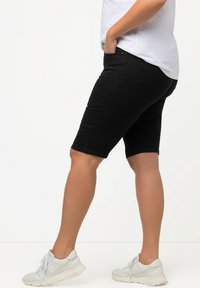 Shorts in denim nero con un design aderente, dotati di tasche laterali e vita media, abbinati a sneaker grigio chiaro.