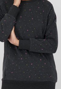 Sudadera gris hecha de tela suave con un patrón de pequeños triángulos multicolores en rosa, púrpura y amarillo. Puños y dobladillo acanalados.