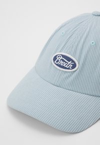 Casquette en velours côtelé bleu clair avec un bord arrondi, comportant un patch ovale brodé blanc avec "Brixton" en texte navy.
