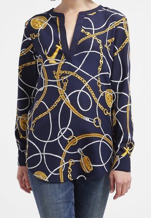 Granatowa bluzka z długim rękawem z motywami złotych łańcuchów, lin i kotwic, zestawiona z niebieskimi dżinsami.