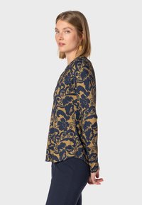 Langarmshirt mit floralem navy Muster auf goldenem Hintergrund. Hat eine entspannte Passform und einen runden Ausschnitt. Weicher Stoff mit leichtem Stretch.