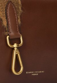 Brown leather bag detail featuring a gold metal clip, brown strap, and the brand name "GIANNI CHIARINI FIRENZE" embossed in white.