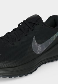 Μαύρο αθλητικό παπούτσι τρεξίματος Nike με υφασμάτινο επάνω μέρος, μαύρα κορδόνια και ανακλαστικό ασημένιο λογότυπο Swoosh στο πλευρό.
