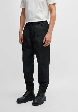 Schwarze, leichte Hose mit elastischem Bund, locker sitzend und mit gerafften Bündchen, kombiniert mit schwarzen Schnürstiefeln mit dicker Sohle.