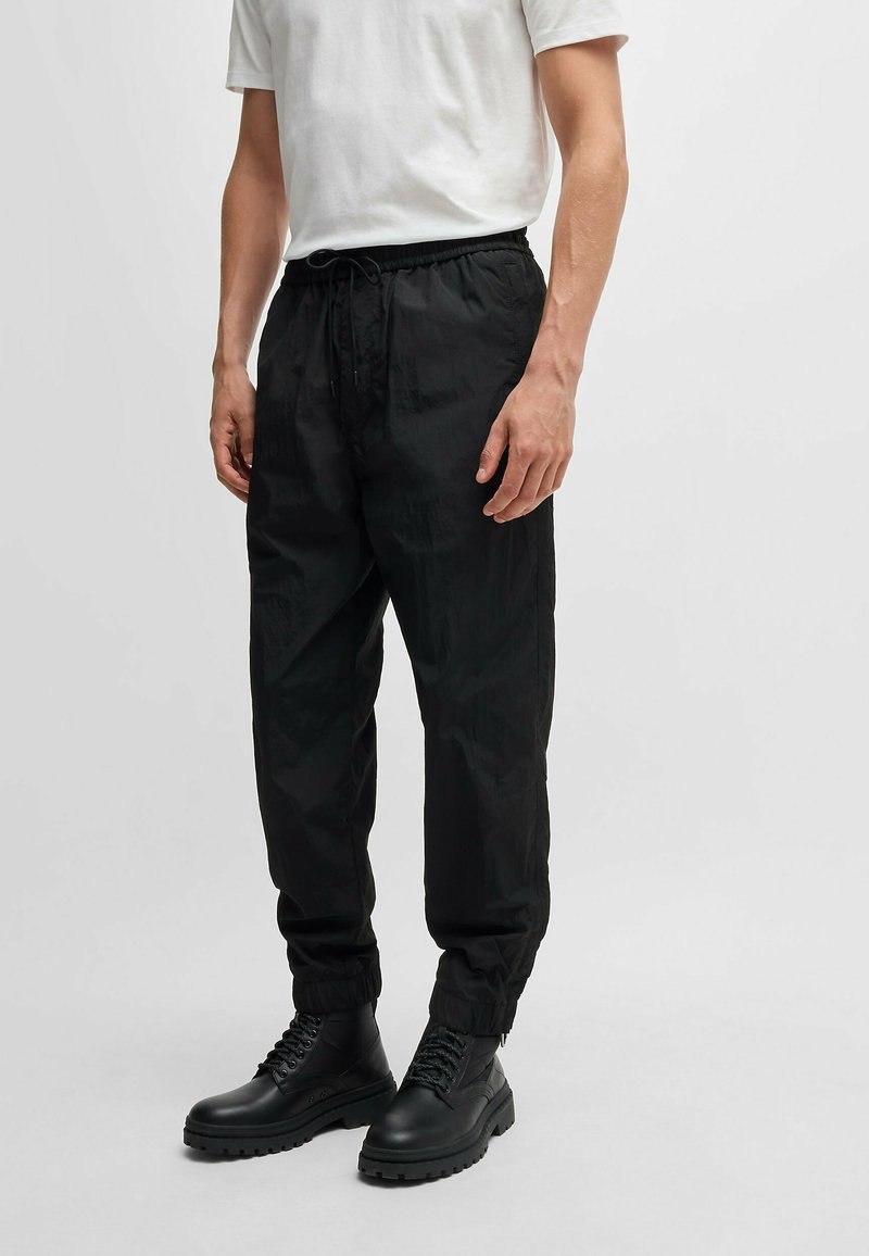 Mustat, kevyet ja joustavat vyötäröhousut rentona istuvuutena ja kerättyinä hihoina, yhdistettynä mustiin nauhakenkäihin, joissa on paksu pohja.