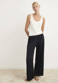 Top de tirantes blanco combinado con pantalones negros de corte holgado, que cuentan con una cinturilla elástica y cordón, fabricados con una tela suave y de textura agradable.