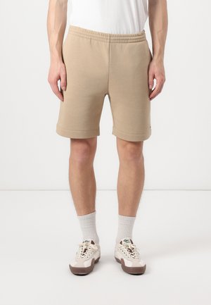 Beige bomuldsblandede shorts med elastisk talje, knælang og med opsmøg. Båret med hvide sokker og sneakers.