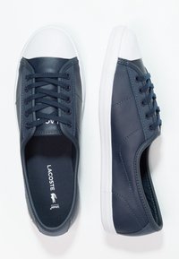 Marinblå sneakers med en slät läderfinish, vit gummitoe cap och snören. Fodret har Lacoste-logotypen i kontrast.