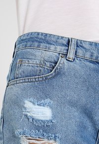 Ljusblå denimshorts med en slitna design, med fransade kanter och en bakficka. Sömmen syns längs midjebandet.