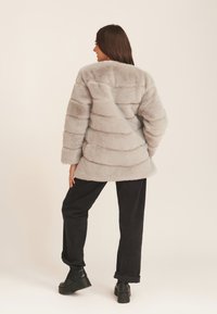 Faux fur coat in light grey with horizontal stripes, oversized fit, and wide sleeves. Paired with black wide-leg pants and platform shoes.