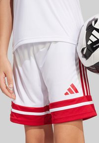 Weiße Sportshorts mit roten Akzenten, ausgestattet mit drei roten Streifen auf jeder Seite und einem Logo. Glattes Material mit weicher Textur.