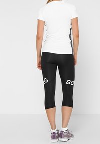 Damski strój sportowy składający się z białej bluzki z krótkim rękawem oraz czarnych legginsów do kostek z perforowanymi detalami i wyraźnym napisem "BOD".