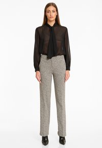 Doorzichtig zwart blouse met een strikdetail, gecombineerd met grijze gestructureerde flared broeken en zwarte puntige schoenen.