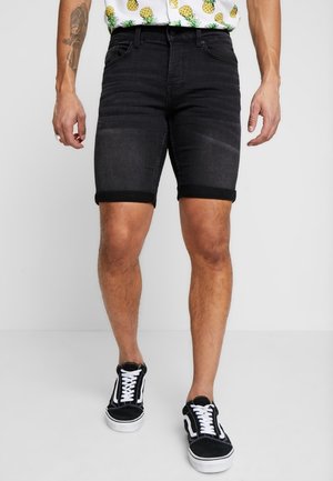 Shorts en denim noir avec des ourlets retroussés, présentant une coupe slim et un léger délavage. Associés à des baskets noires et une chemise à motifs.