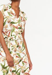 Sukienka krótko rękawowa z białej tkaniny z kwiatowym i zwierzęcym nadrukiem. Z paskiem w talii i guzikami wzdłuż przodu.