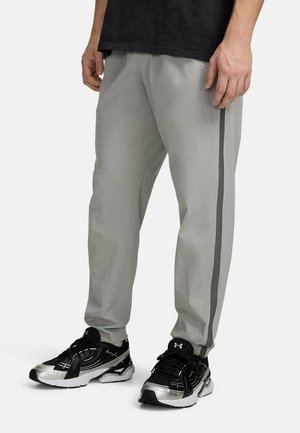 Lichtgrijze sportbroek met een gestructureerde stof, een slanke pasvorm en contrasterende donkergrijze zijstrepen, gecombineerd met zwarte en zilveren sneakers.