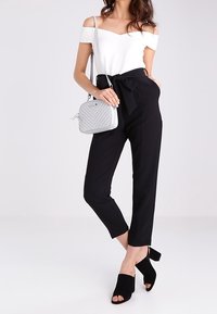Top bianco scollato abbinato a pantaloni neri a vita alta, borsa grigia strutturata e tacchi aperti neri. Tessuto liscio e vestibilità sartoriale.