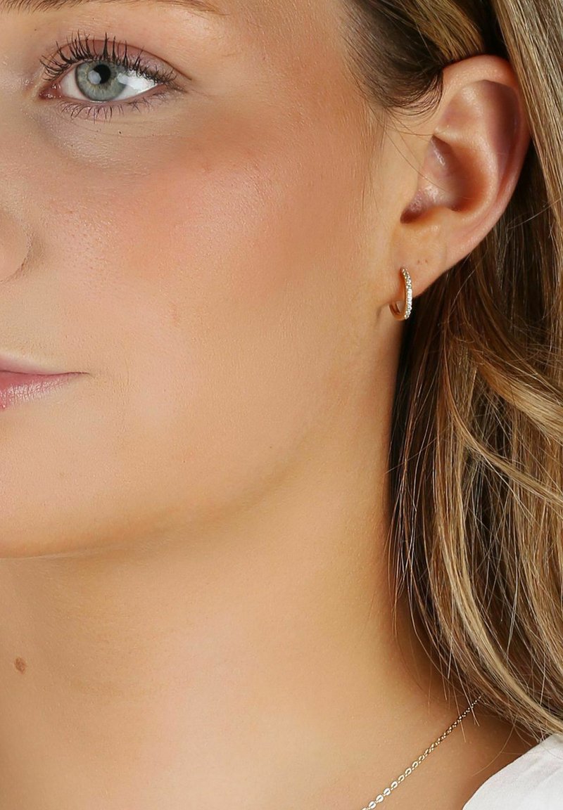 Guldörhänge med en strukturerad yta, prytt med små klara ädelstenar längs framkanten som ger en subtil glittring.