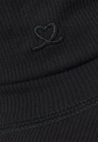 Tissu noir à côtes présentant une contour de cœur brodé en noir. La texture est douce avec un léger éclat, et comprend des détails de couture visibles.