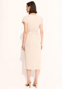 Beżowa sukienka do kolan z krótkimi rękawami, dopasowaną talią z paskiem oraz gładką fakturą. Tył ma subtelny detal szwu.