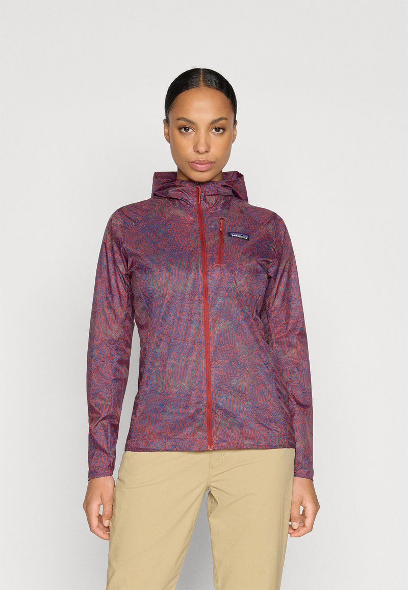 Chaqueta ligera con cremallera en rojo y azul con un patrón, capucha, mangas largas y un pequeño bolsillo frontal. Tejido texturizado con un diseño ajustado.