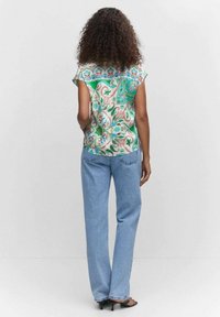 Blusa de manga corta con estampado en diseño paisley verde y crema; combinada con jeans rectos de un azul claro. Vista trasera, detalles de textura mínimos.