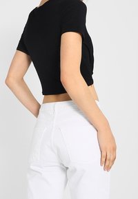 Černé cropped tričko s krátkým rukávem, spárované s bílými džínami s vysokým pasem, které mají zadní kapsy a švy.