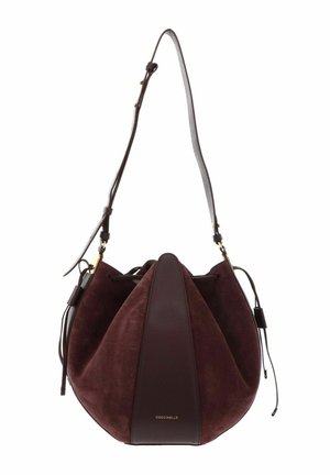Sac seau en daim et cuir marron foncé avec bandoulière réglable et fermeture par cordon, orné d'un petit logo doré Coccinelle.