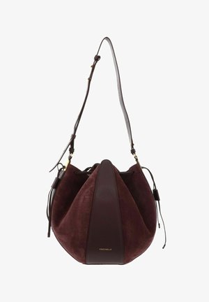 Sac seau en daim et cuir marron foncé avec bandoulière réglable et fermeture par cordon, orné d'un petit logo doré Coccinelle.