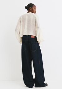 Lässig geschnittene dunkle Denim-Jeans mit roten Nähdetails, kombiniert mit einer leichten cremefarbenen Bluse mit Ballonärmeln.