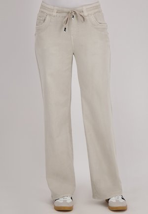 Beige wijde broek met een trekkoord in de taille, twee voorkruiden en een gladde, gestructureerde stof. Draagt met witte en grijze sneakers.