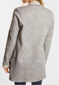 Ljusgrå, strukturerad lång jacka med diamantmönster, långa ärmar och rundad nederkant med en dold sömmavslutning.