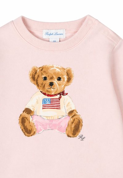 T-shirt rose pour bébé avec un ours en peluche portant un pull blanc avec un drapeau américain et un pantalon rose, étiqueté Ralph Lauren 6M.