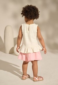 Valge ja beež ruuduline top volangiliste servadega, kihiline roosa puuvillase seelikuga. Tagaküljel nööpidega kinnitusega. Pruunid sandaalid.