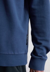 Granatowy sweter z miękkiego materiału, z prążkowanymi mankietami i dołem. Posiada małą metkę Marc O'Polo z boku.