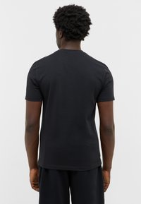 T-shirt noir à manches courtes dans une coupe décontractée, fabriqué en coton. Texture lisse avec un col rond et sans motifs ni graphismes visibles.