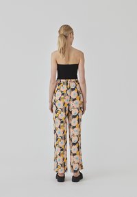 Pantalones anchos de flores en rosa, negro y amarillo con cintura elástica. Combinados con una blusa negra sin tirantes y zapatos negros.