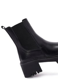 Bottine en cuir noir avec panneaux élastiques sur les côtés, surface texturée, talon épais et coutures renforcées pour une durabilité accrue.