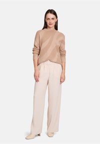 Beiger Strickpulli mit abstrakten Mustern, kombiniert mit hellbeigen weit geschnittenen Hosen und beigen Stiefeletten. Weiche Textur, lässiger Schnitt.