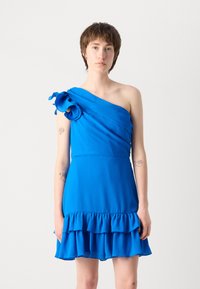 Robe bleue à une épaule avec tissu drapé, ourlet volanté et matière texturée. Présente un accent floral sur l'épaule et un corsage cintré.
