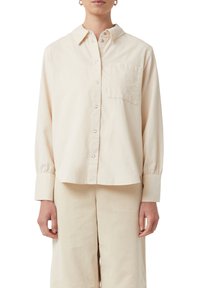 Camicia beige con bottoni realizzata in tessuto morbido, con colletto classico, taschino sul lato sinistro del petto e maniche lunghe con polsini. Design semplice.