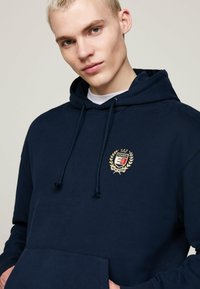 Felpa blu navy in cotone, con tasca a marsupio, cordini e un logo ricamato con design di alloro.