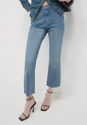 Light blue denim jeans with a straight-leg cut and frayed hem, paired with black strappy high-heeled sandals.