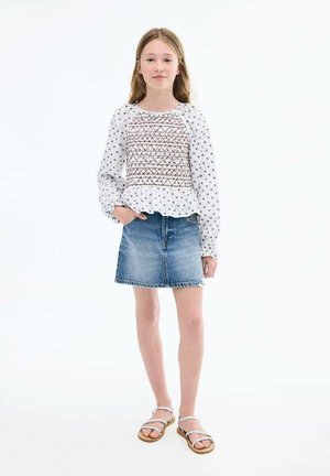 Weiße Bluse mit langen Ärmeln und gemustertem Stickereien, Peplum-Saum, kombiniert mit einem Jeansrock. Braune Sandalen mit Riemchen runden das Outfit ab.